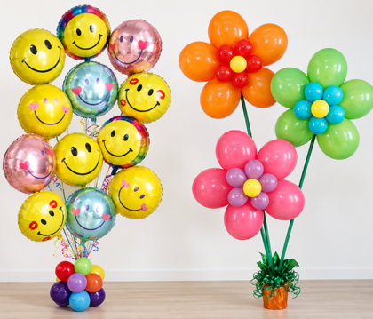Colorful smiley face Mylar balloon bouquet alongside orange, pink and green balloon flower arrangements on a white background.